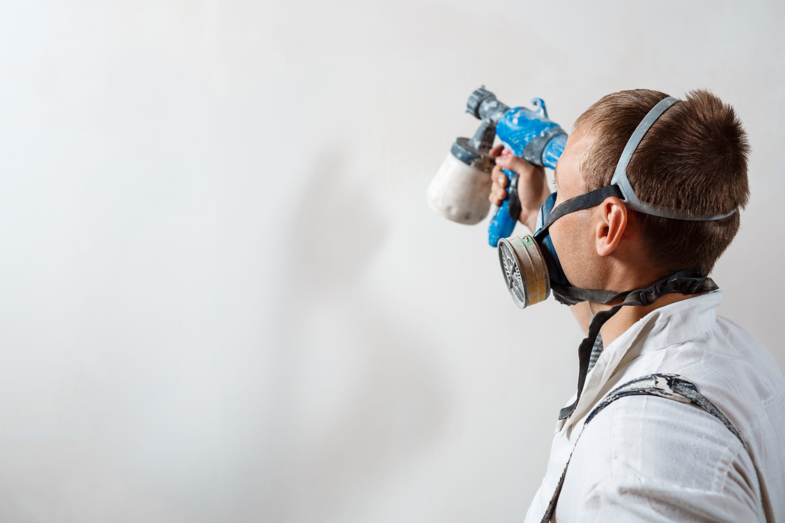 Worker painting wall with spray gun in white color. Copy space.